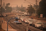 A long line of cars not moving on a winding road with bushfire smoke in the air.