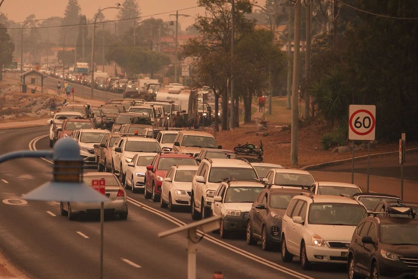 A long line of cars not moving on a winding road with bushfire smoke in the air.