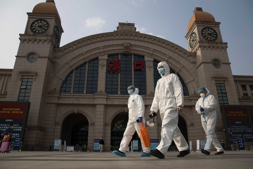Workers in protective suits walk past the Hankou railway station.
