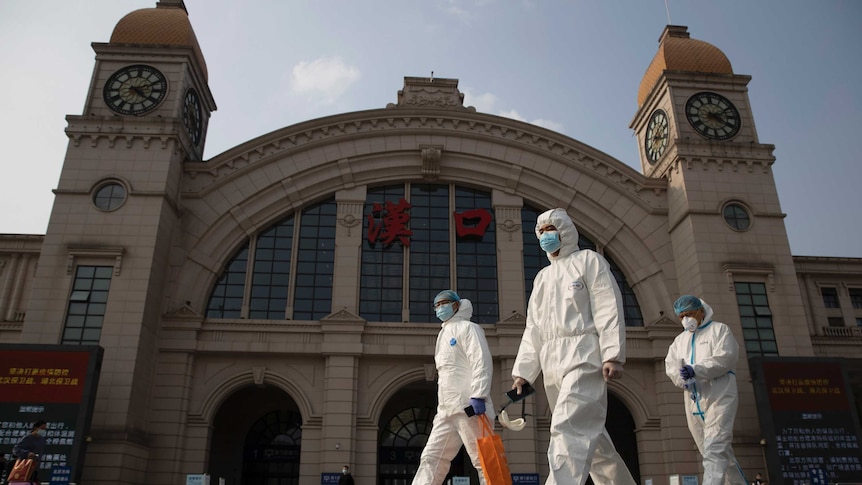 Workers in protective suits walk past the Hankou railway station.