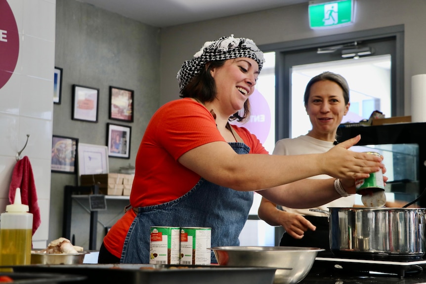 Two women working in a kitchen smiling.