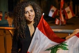 A Lebanese woman smiles while holding a Lebanese flag