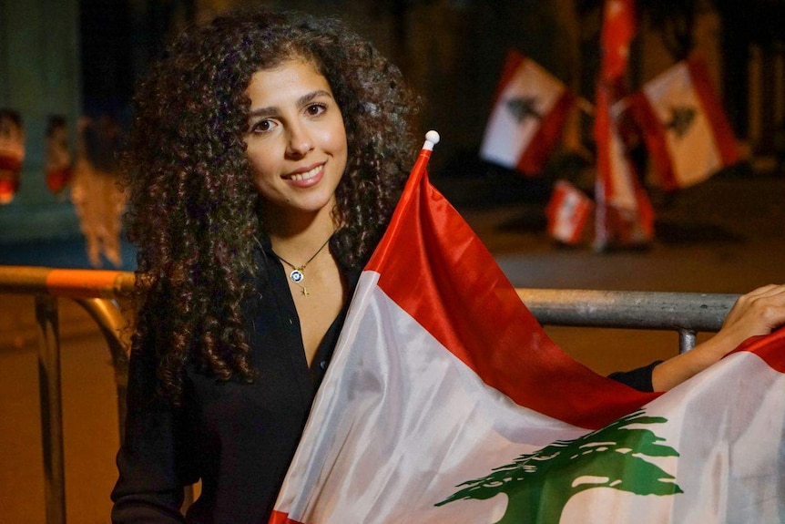 A Lebanese woman smiles while holding a Lebanese flag