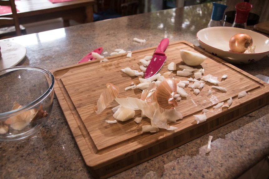 Pieces of onion and skins scattered across a chopping board and bench.