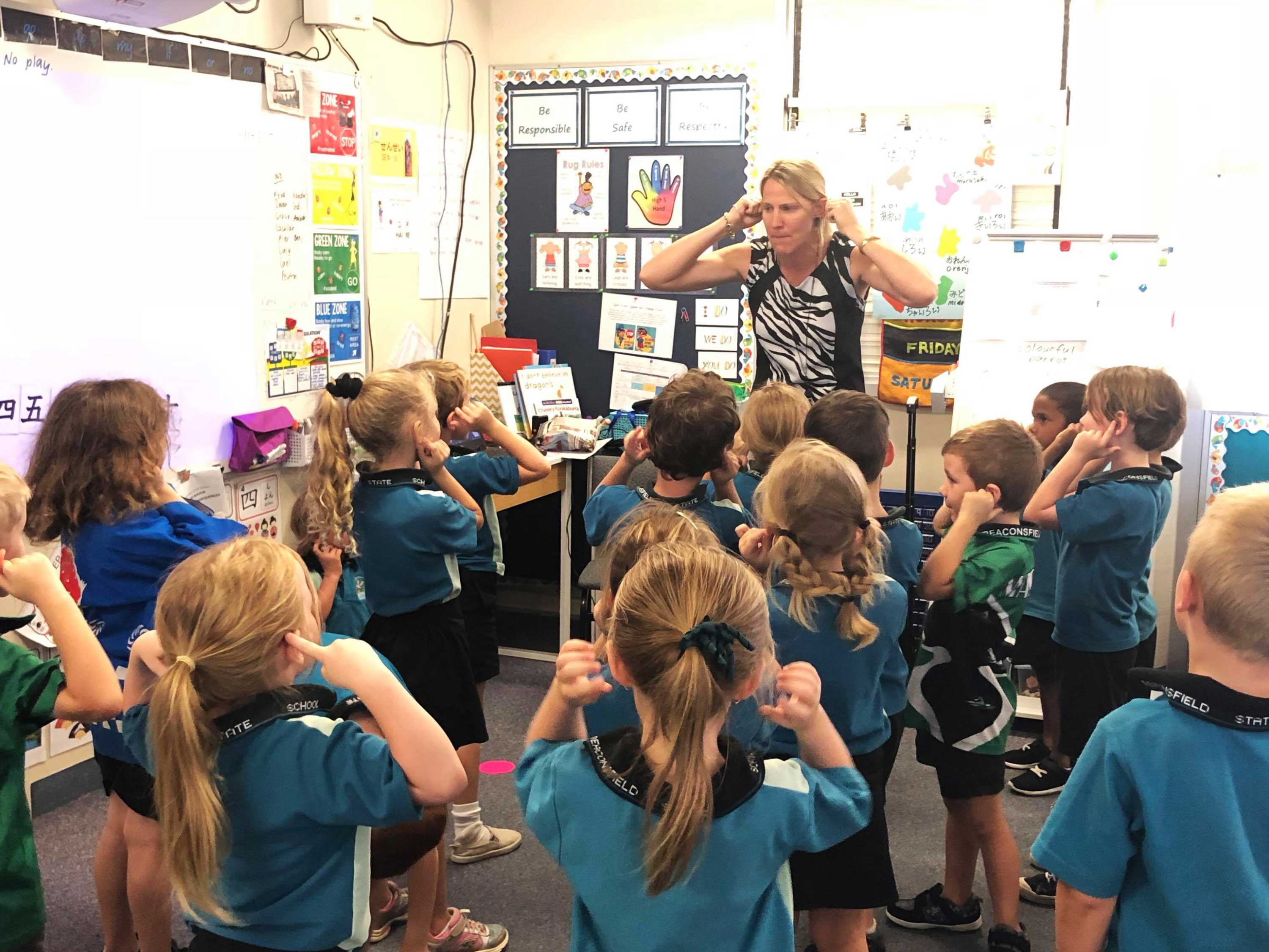 A teacher at the front of a classroom sings a song with young children.