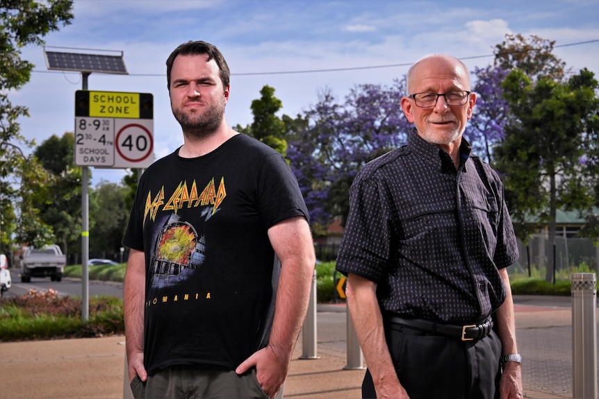 Two men stand next to a school zone sign