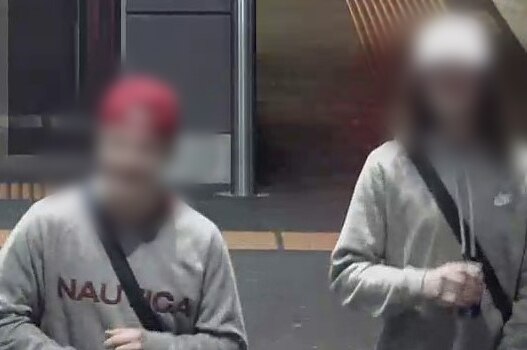 Two young males on CCTV footage, one wearing a red cap and one wearing a white cap. Both are wearing grey hoodies.