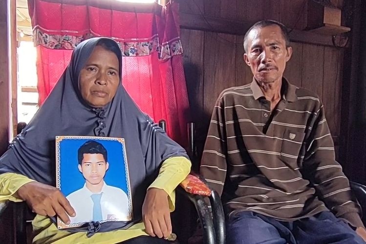 An older Indonesian couple hold a school photo of their son.