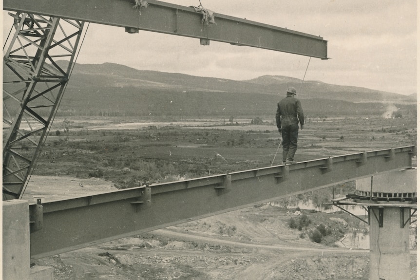 A man walks along a steel beam on a dam construction site.