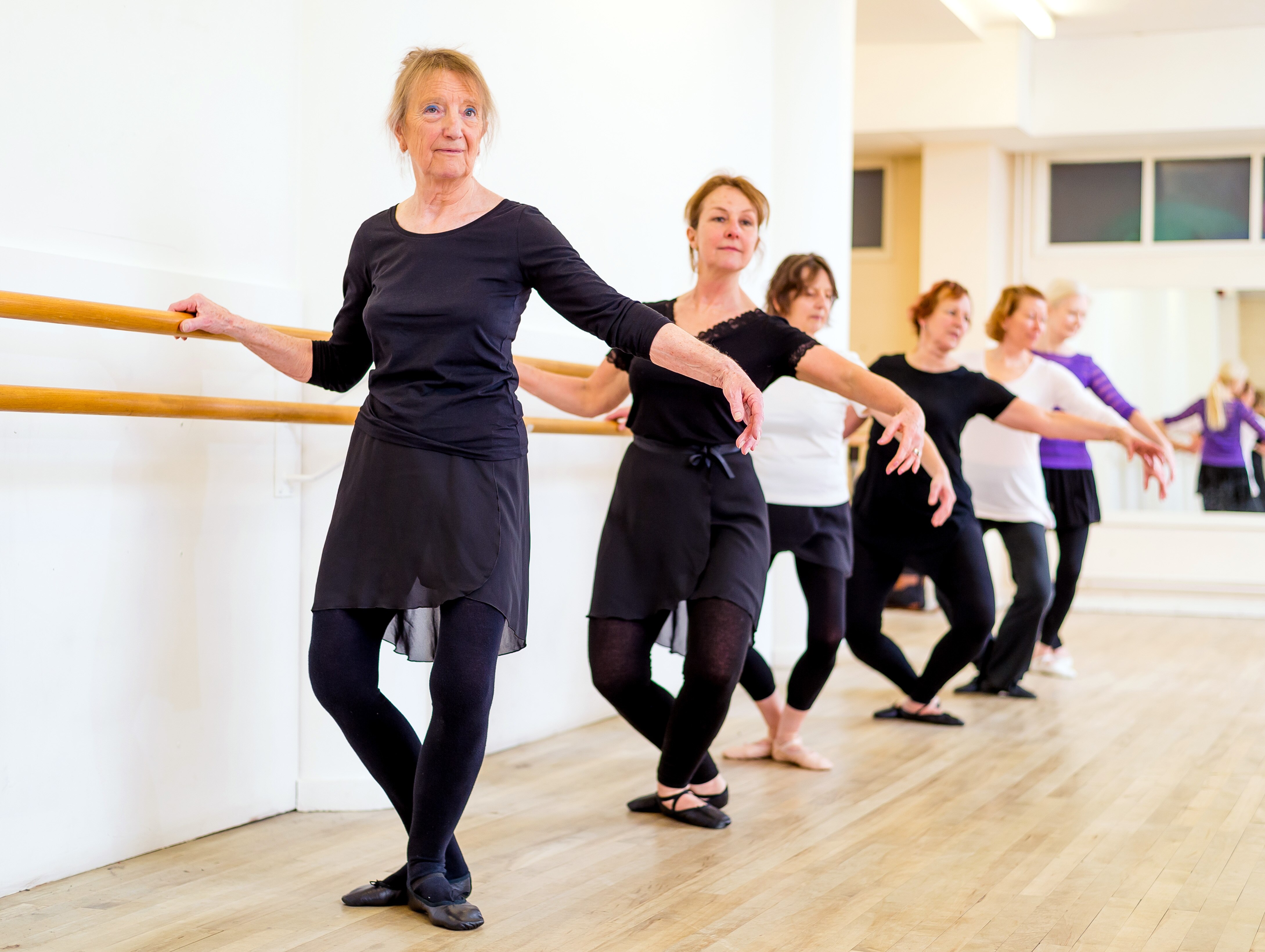 Six women do a plie at the bar. 