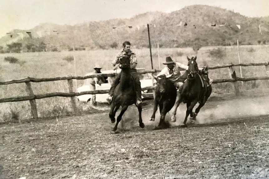 One man on horseback, second man diving off his horse onto a steer in rodeo arena.
