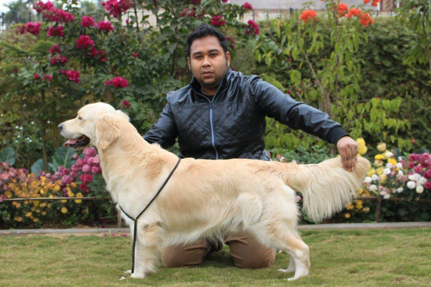 Abhijeet Nath kneels on grass infront of a flower garden, posing with a golden reviever or labrador dog