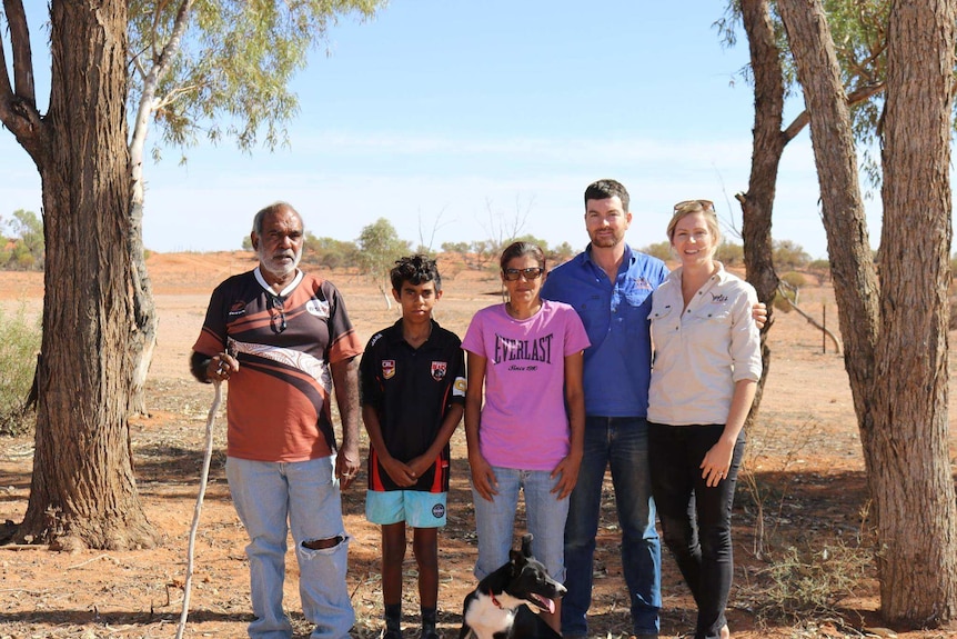 Five people pose for the camera in front of an arid landscape.