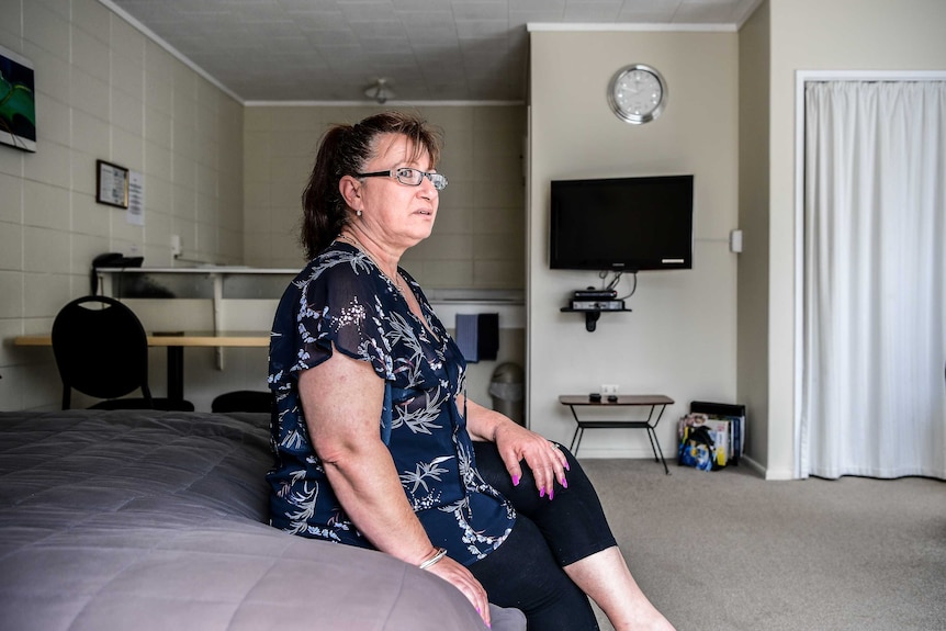 A woman sitting on a motel bed looking solemn