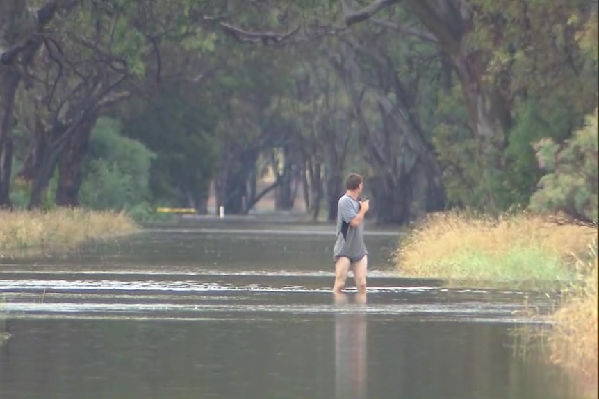 A person wades through water over a flooded road.