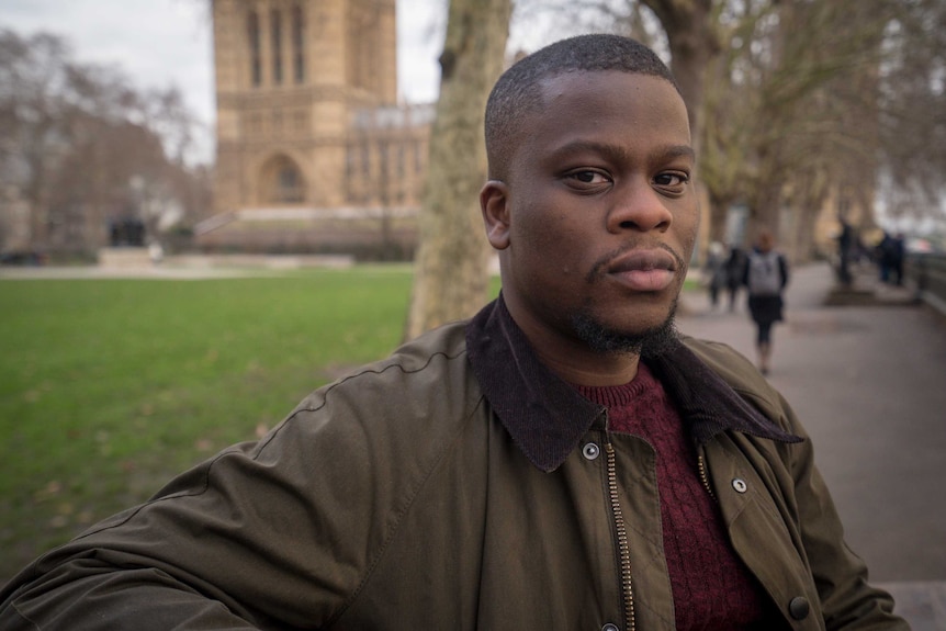 A black man wearing an olive jacket stands outside a cathedral