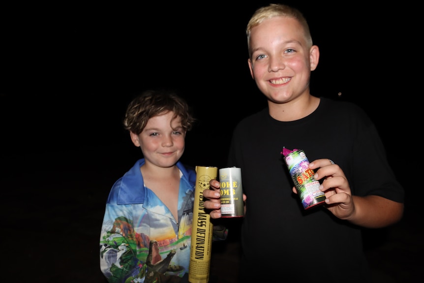 Two young boys holding fireworks on a beach at night