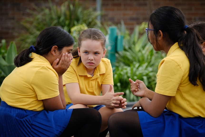 Three young primary school aged girls talking in a circle.