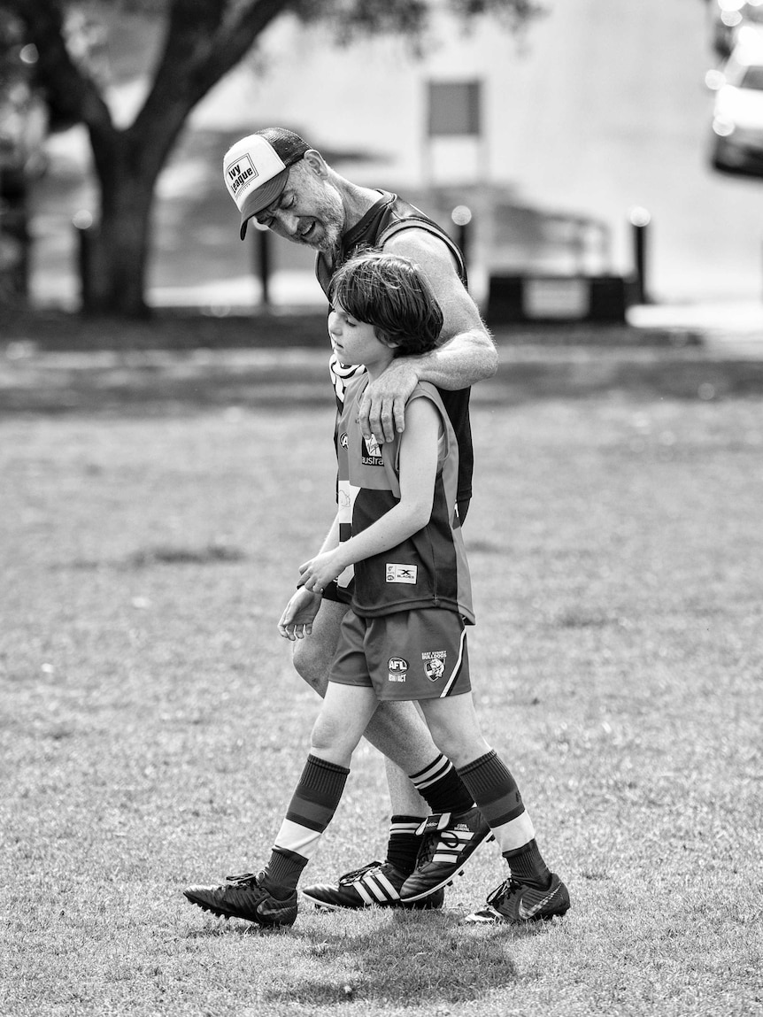 A father and son walk together during a match of Aussie Rules.