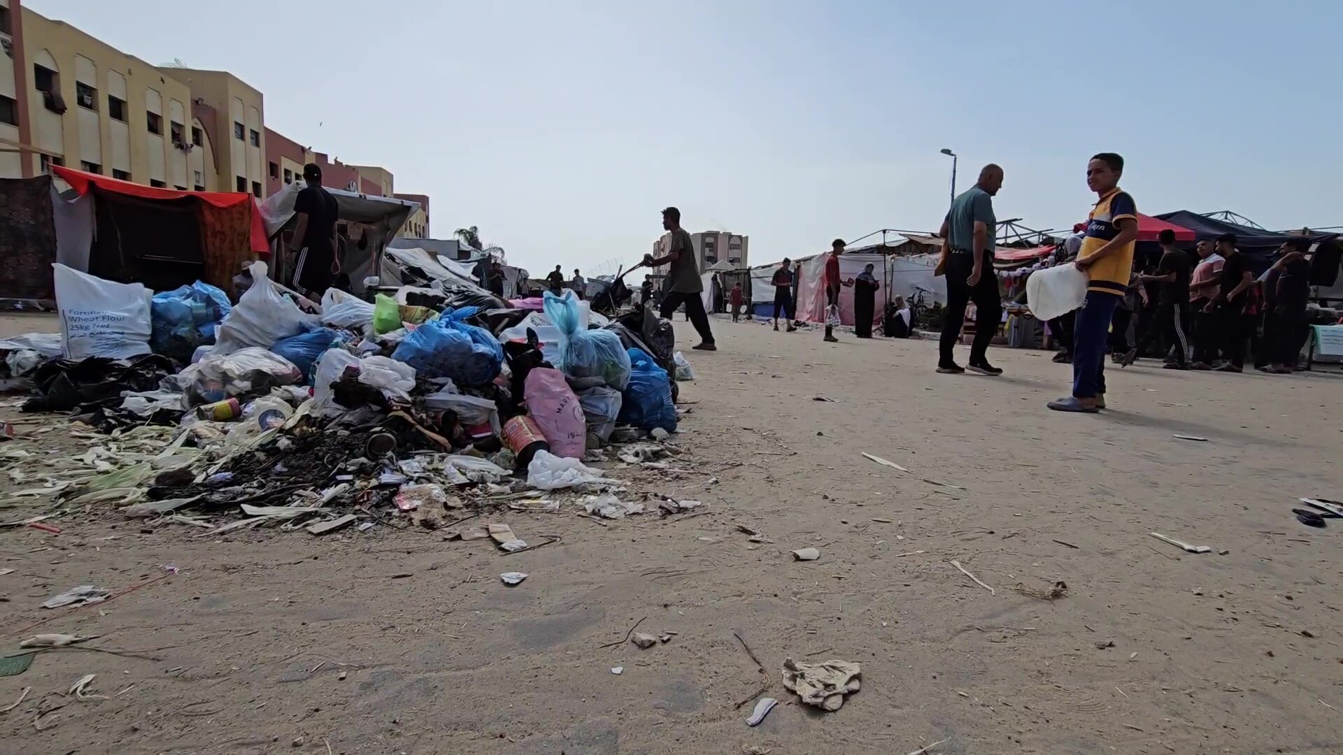 A pile of trash in the middle of a dirt road with people walking around it