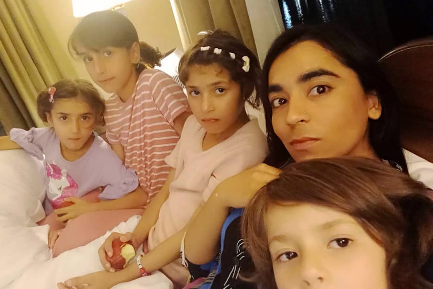A woman and four children sit together on a bed. 