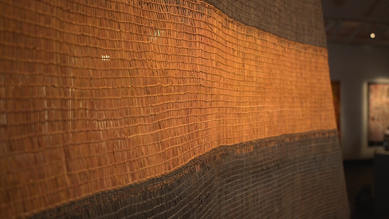 A photograph of an orange and black woven sail