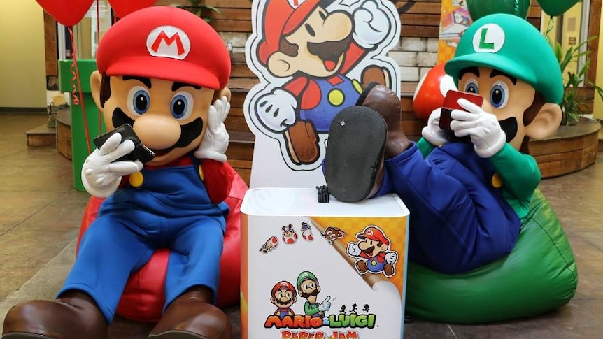 Nintendo game characters Mario and Luigi sitting on beanbags playing a handheld game.