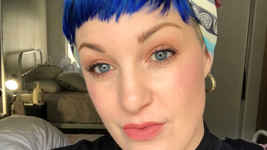 A woman with short, blue hair wearing a multicloured bandanna 