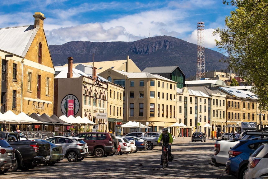 A man on a bike rides through Salamanca Place with Mt Wellington in the background.