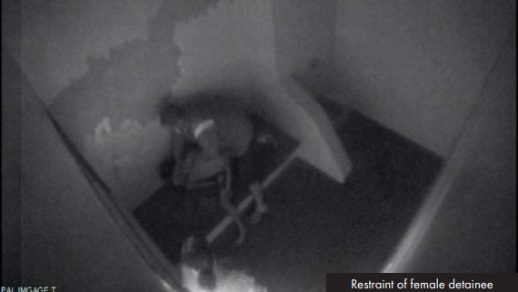 CCTV footage of a guard holding a female detainee down onto a bed