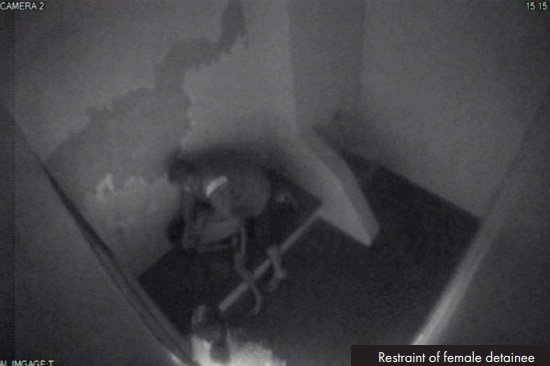 CCTV footage of a guard holding a female detainee down onto a bed