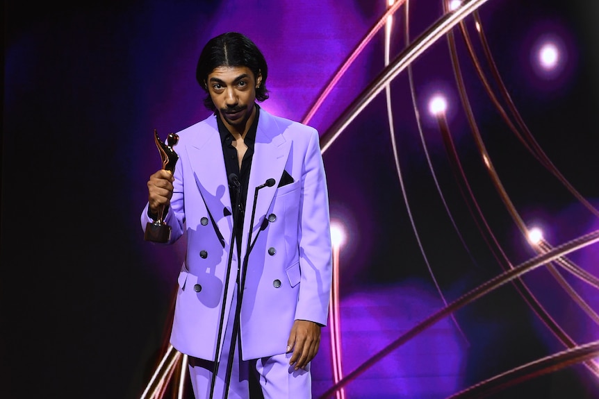 A man wearing a purple suit holding a golden award in his hand