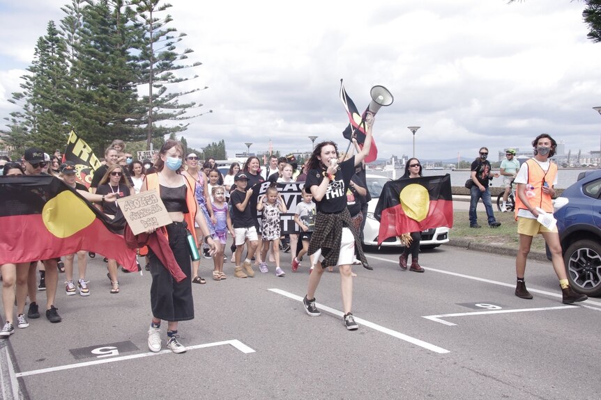 A group marching on the street carrying and wearing the Aboriginal flag.