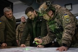 A group of four men, two in military uniforms and one wearing a helmet, lean over a table while studying a map.