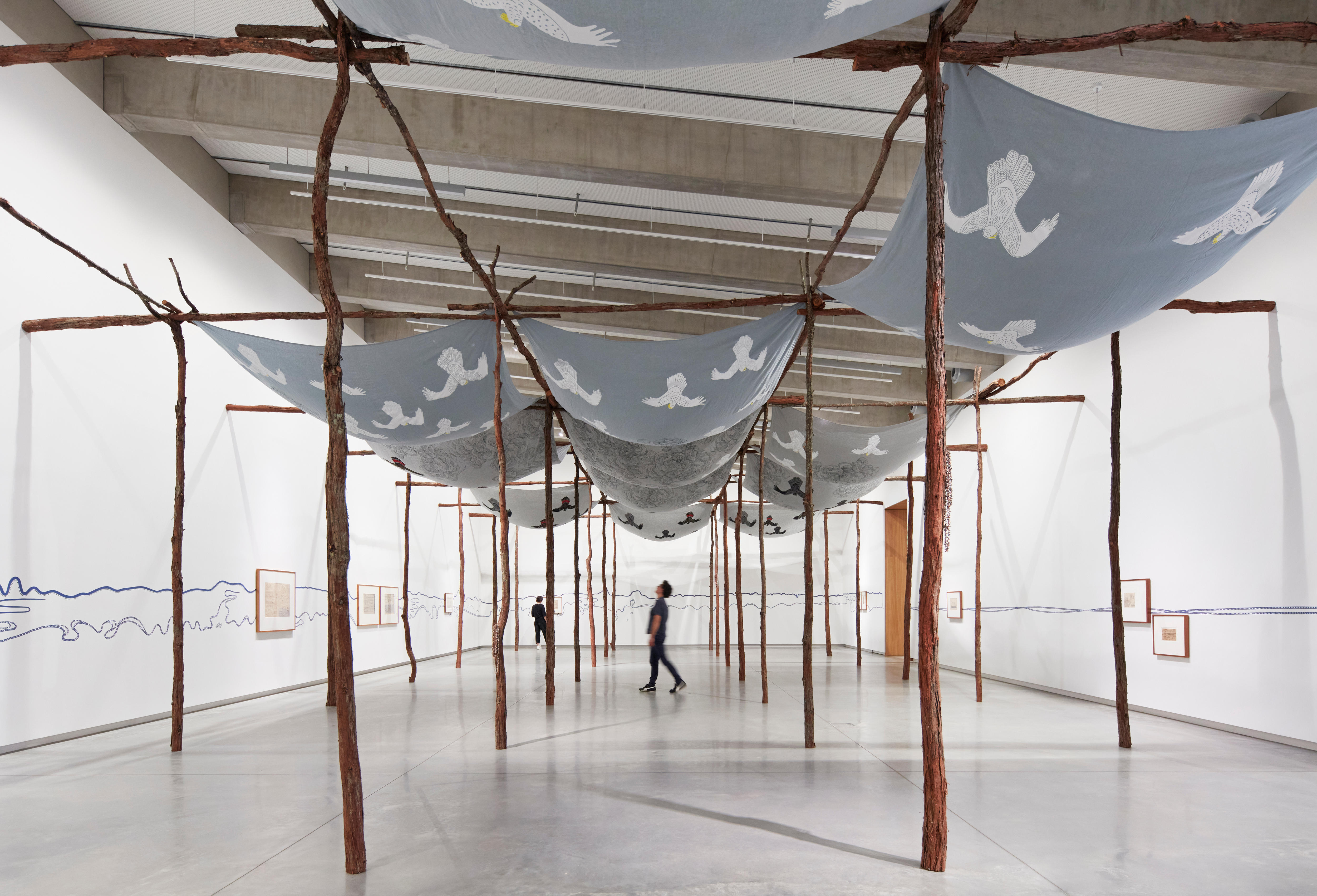 A large-scale architectural gunyah structure made from turpentine trees. Suspended from the gunyah are screen-printed skyscapes.
