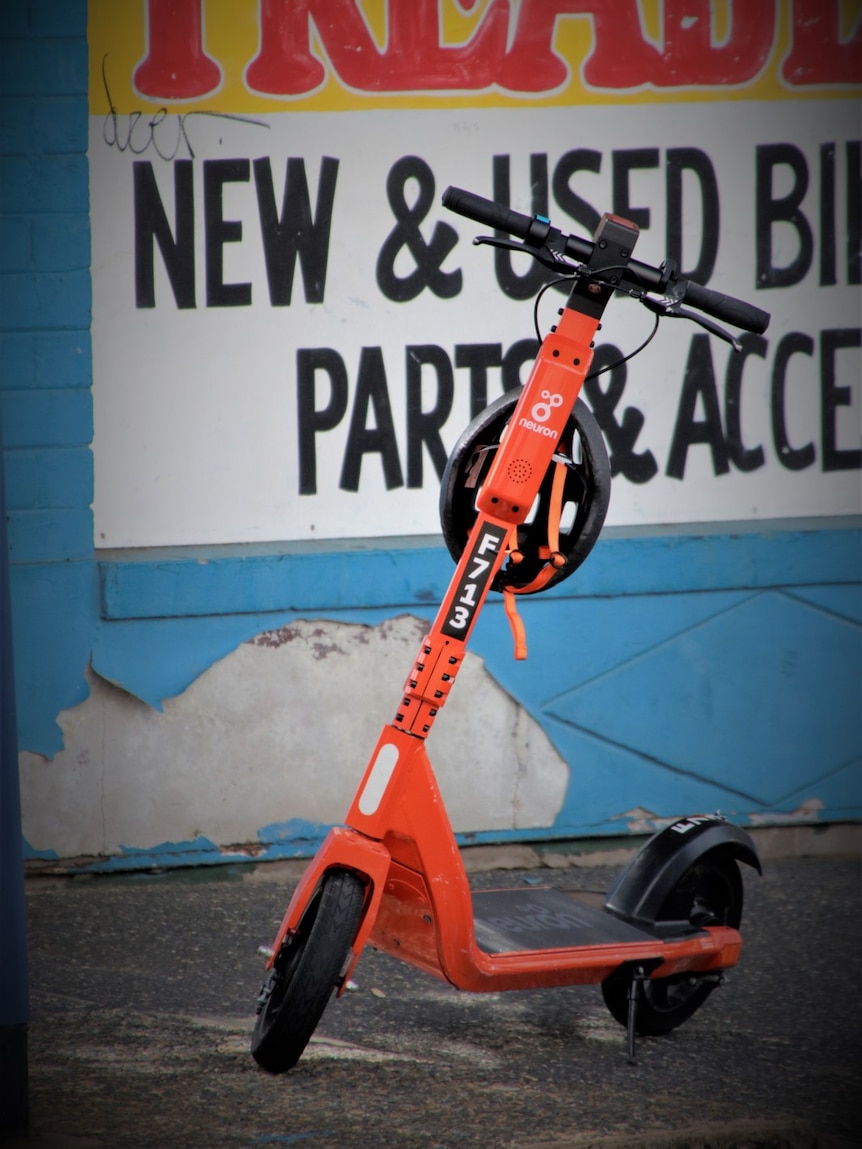 A photo of a bright orange e-scooter parked in front of a shop in Darwin city.