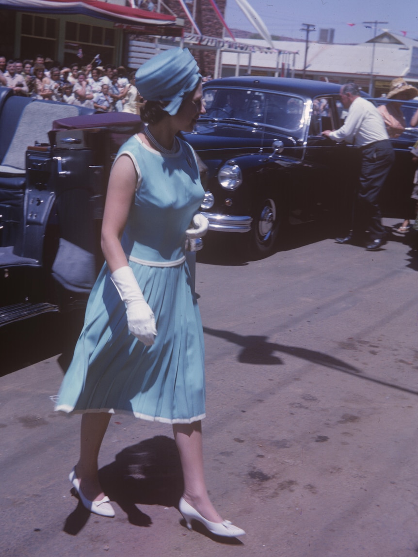 Archival image of Queen Elizabeth II wearing a pale blue dress with white gloves in an Alice Springs street.
