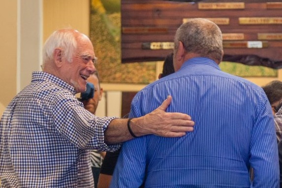 A man places his arm around the back of another man inside the cafe.