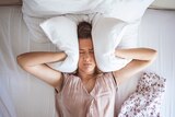 Woman in bed with a pillow pressed to her ears 