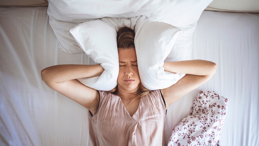 Woman in bed with a pillow pressed to her ears 