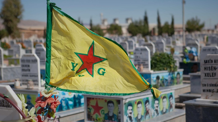 A Kurdish flag flies on top of a tomb stone.