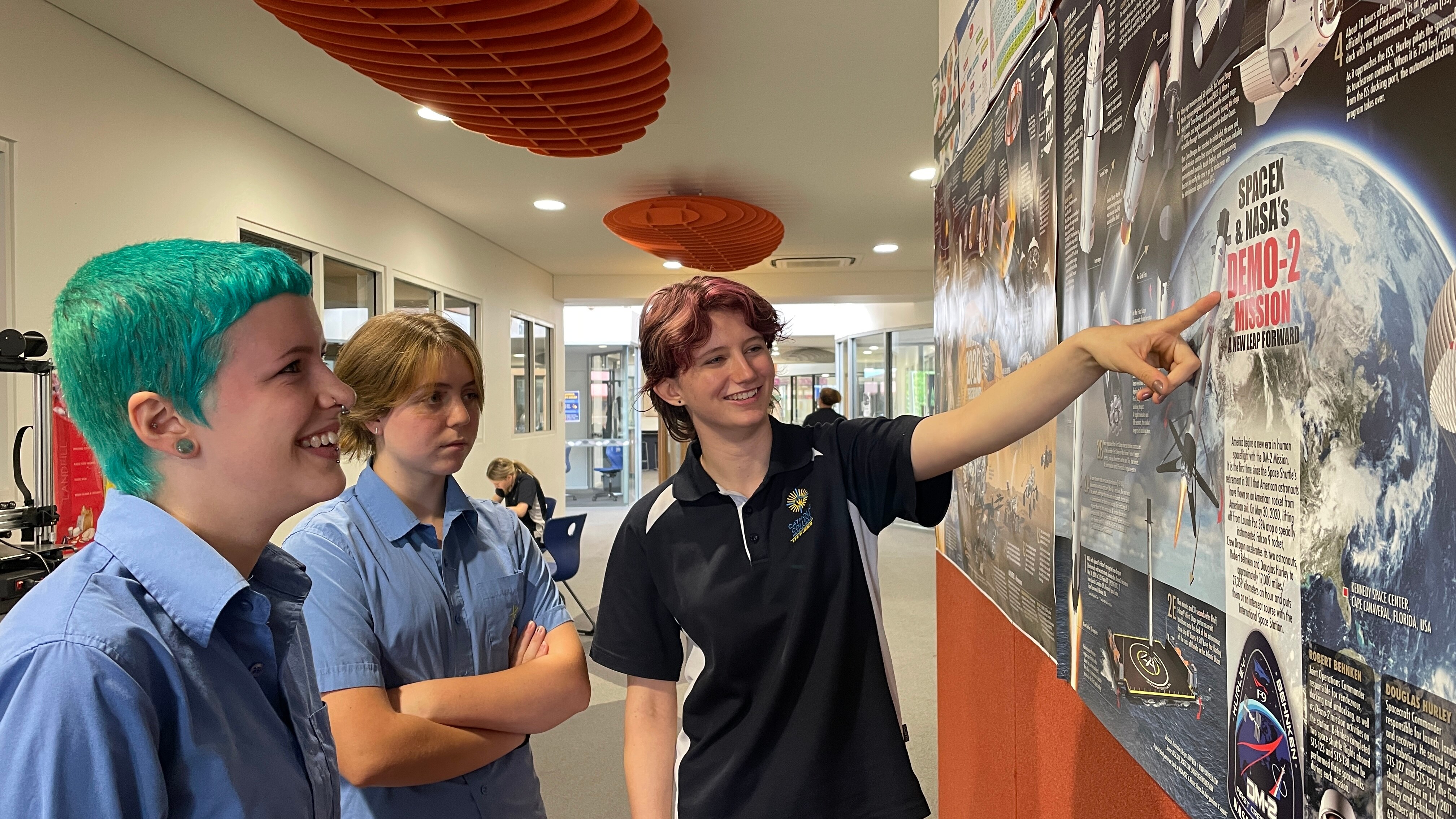 Three people look at a poster, one is pointing