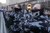 A man wearing a balaclava with a skull print stands at the front of a far-right protest in Ukraine.