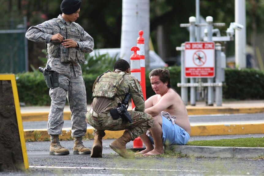 Two people in military fatigues tend to a man with his shirt off sitting on a curb.