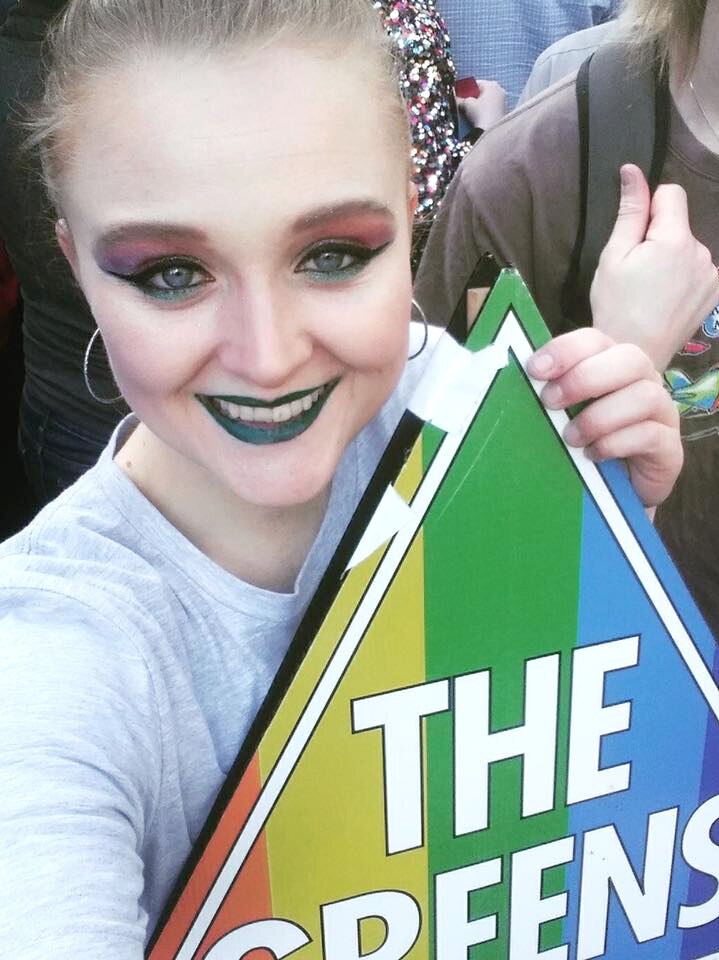 Young woman holding a Greens rainbow sign.