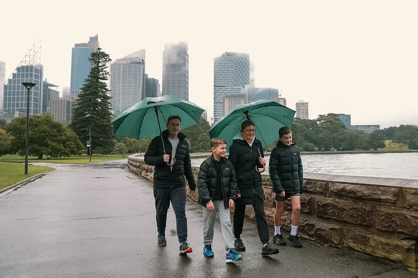 a family of four people, a man, a woman and two young males walk in the rain carrying umbrellas