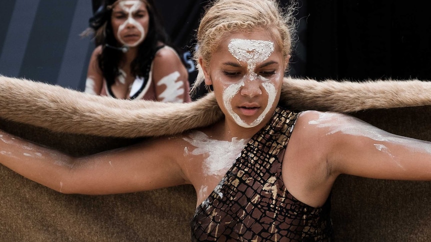 A young Indigenous woman with face paint stands in front of a banner at Yabun.