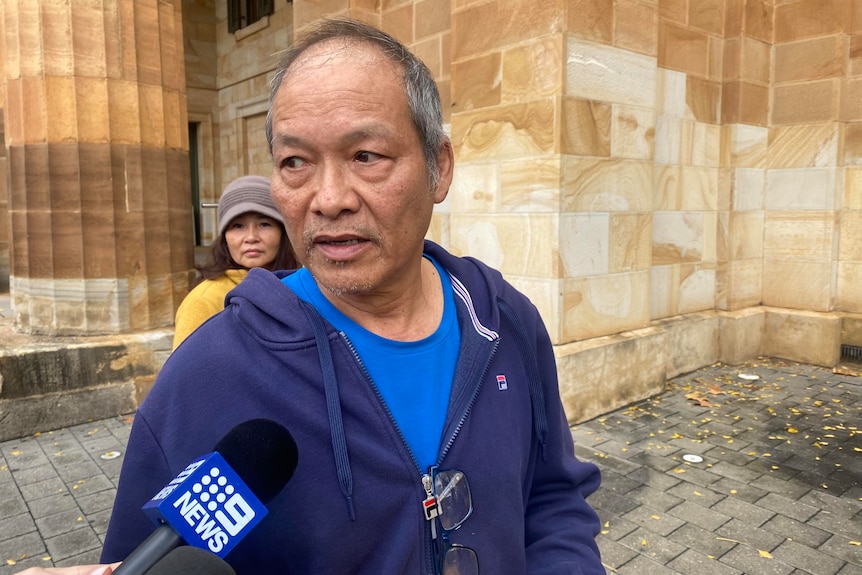 A man in blue top outside a court building. A woman looks on behind him