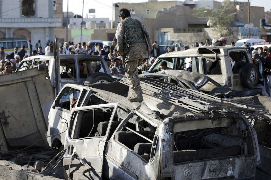 A Houthi fighter walks on a vehicle damaged by an air strike