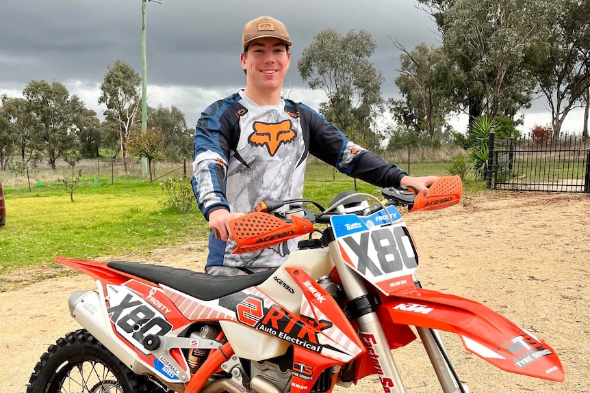 smiling man holding handle bars of orange and white dirt bike